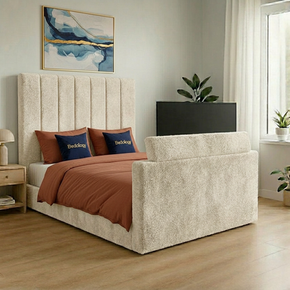 An upholstered bed frame with a tall channel-tufted headboard and matching footboard, shown in a styled bedroom. The bed is dressed in sage green bedding and two matching pillows, set against a light gray wall with a wooden floor.